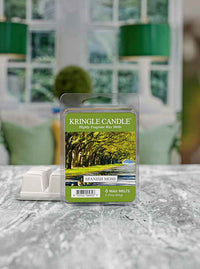 Pack of Kringle Candle Spanish Moss wax melts on a textured surface with a blurred, green-themed room in the background.
