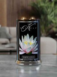 Lit candle with white lotus image on label. Black container reads "Kringle Candle, White Lotus." Indoor setting in backgro…
