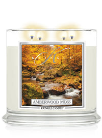 Lit XL 4-wick candle, Amberwood Moss. Label features an autumn forest with a flowing stream among mossy rocks.