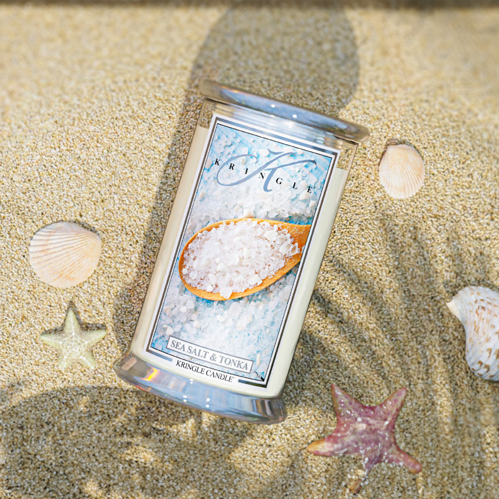 Kringle Candle’s Sea Salt & Tonka large jar candle resting on sunlit sand, surrounded by seashells.