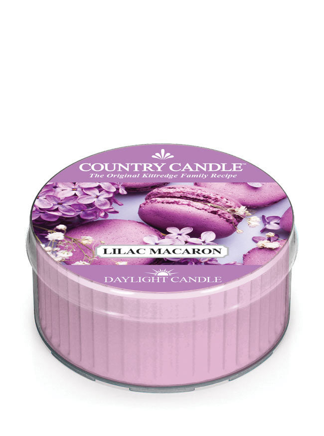 Round lilac-colored candle with a lid featuring lilac macarons and flowers. Text reads "Country Candle, Lilac Macaron."