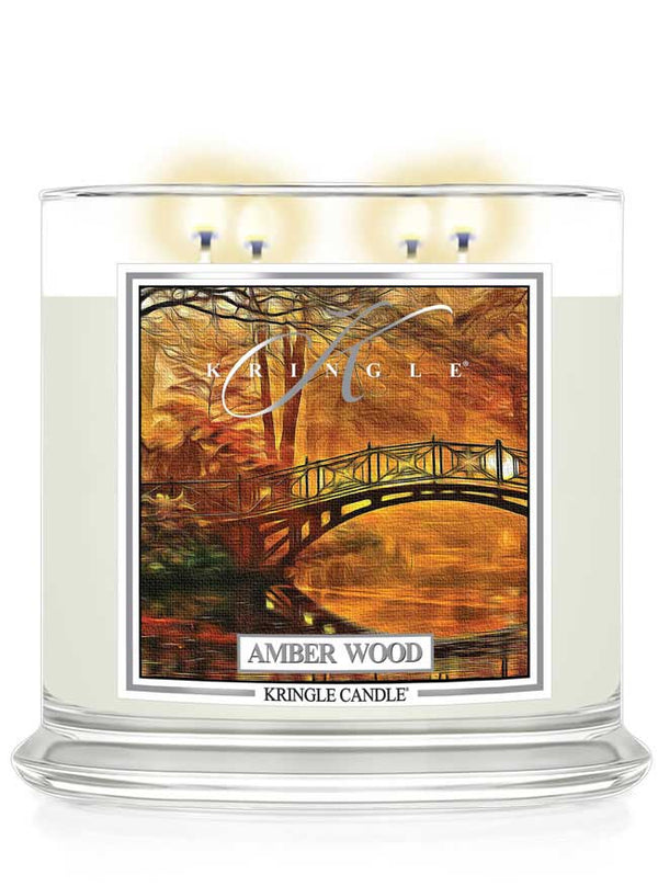Kringle Candle lit 4-wick in Amber Wood scent with a scenic label on a white background