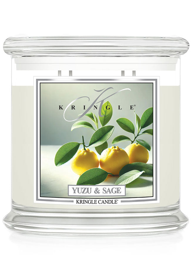 A clear glass candle labeled "Yuzu & Sage" with an image of yellow yuzu fruit and green leaves on the front.