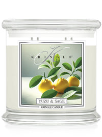 A clear glass candle labeled "Yuzu & Sage" with an image of yellow yuzu fruit and green leaves on the front.