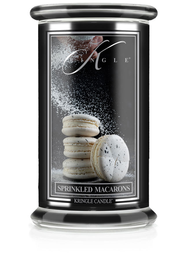 A black candle jar labeled "Kringle Candle" features an image of stacked macarons with powdered sugar being sprinkled.