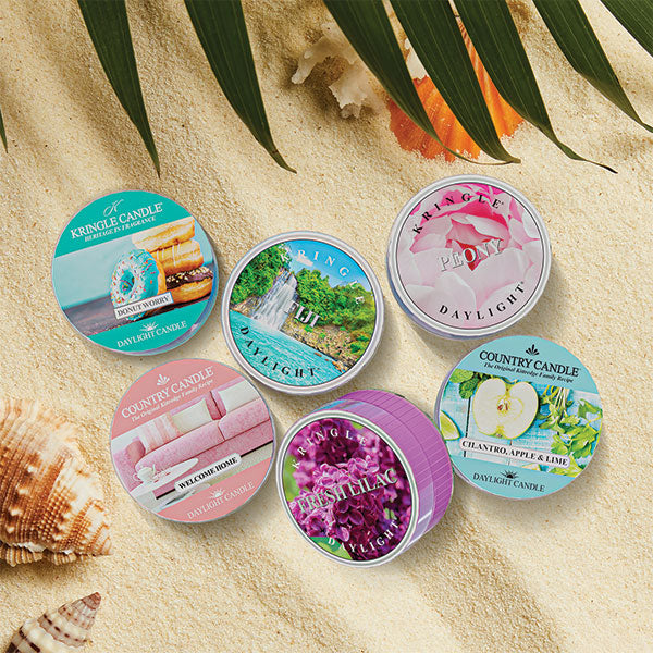 Summer DayLight Candles, what are twice the size of a tea light, shown on a sandy beach with seashells and palm leaves