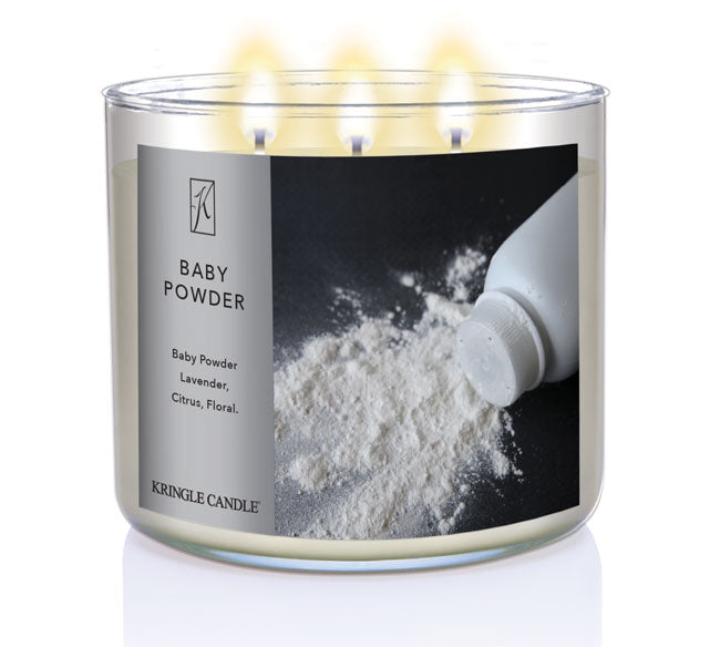 A three-wick lit candle in a clear glass jar with a classic powder-themed label. The candle’s wax is soft white, and all three wicks are burning.