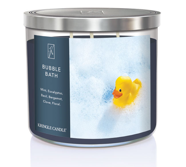 A three-wick candle in a clear glass jar with a silver lid and a calming bath-themed label. The label features a rubber duck floating in a sea of white bubbles. The candle’s wax is dark blue, and the wicks are unlit. The scent notes listed are mint, eucalyptus, basil, bergamot, clove, and floral.