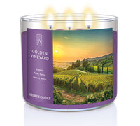 A three-wick lit candle in a clear glass jar with a scenic vineyard-themed label. The candle’s wax is deep purple, and all three wicks are burning.