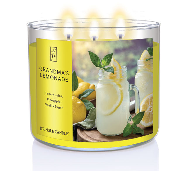A three-wick lit candle in a clear glass jar with a refreshing drink-themed label. The candle’s wax is bright yellow, and all three wicks are burning.
