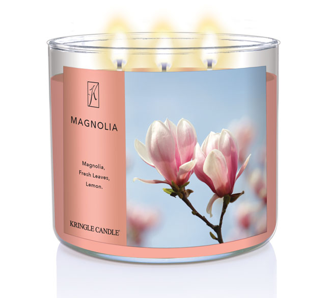 A three-wick lit candle in a clear glass jar with a soft floral-themed label. The candle’s wax is a warm peach shade, and all three wicks are burning.