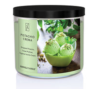 A three-wick candle in a clear glass jar with a gold lid and a creamy dessert-themed label. The label features a bowl of pistachio gelato topped with chopped nuts and a swirl of caramel. The candle’s wax is soft green, and the wicks are unlit. The scent notes listed are pistachio, pralines, and sugared vanilla cream.
