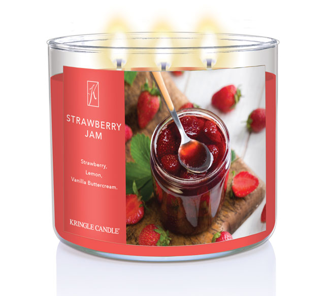 A three-wick lit candle in a clear glass jar with a sweet jam-themed label. The candle’s wax is deep red, and all three wicks are burning.