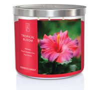 A three-wick candle in a clear glass jar with a gold lid and a vibrant floral-themed label. The label features a lush tropical arrangement of hibiscus flowers, bright pink and red petals, and green leaves. The candle’s wax is hot pink, and the wicks are unlit. The scent notes listed are hibiscus, strawberries, and fruit punch.