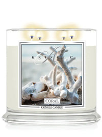 Lit Kringle Candle in Coral scent with glowing flames and label showing white coral on a beach background.