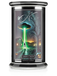 Unlit Halloween candle labeled "Abduction." The label shows a UFO abducting a person near a farmhouse with glowing lights.