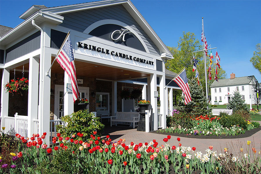 Kringle Candle Company Retail Store in summertime with tulips and US flags hanging in pole brackets and flagpole.