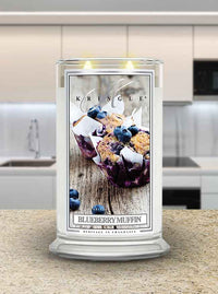 Photo of Kringle Candle's Blueberry Muffin scented candle in a large 22oz glass jar with both wicks lit sitting on a kitchen counter.