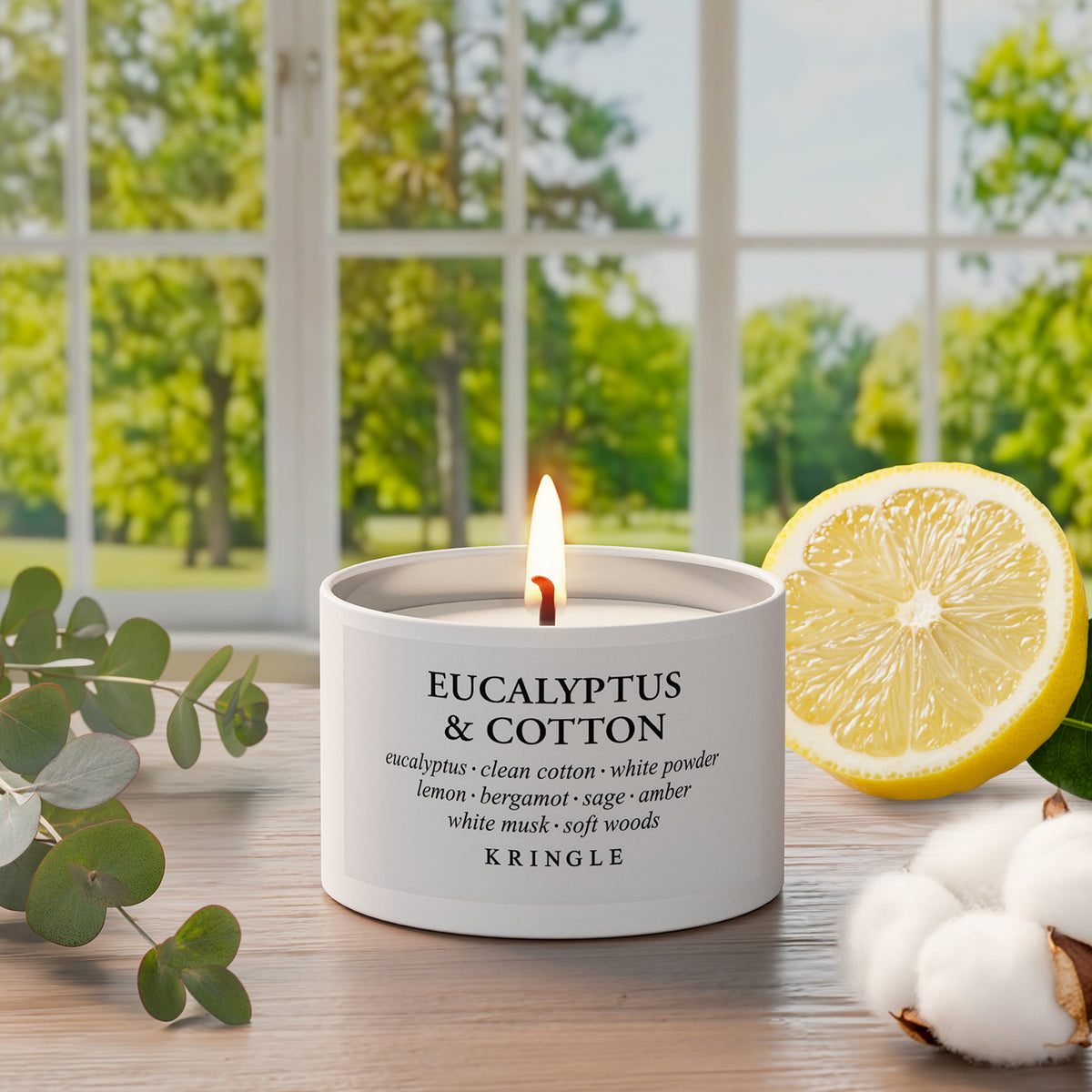 Kringle Candle tin labeled 'Eucalyptus & Cotton' on a table with lemon and cotton and window and greenery in the background.