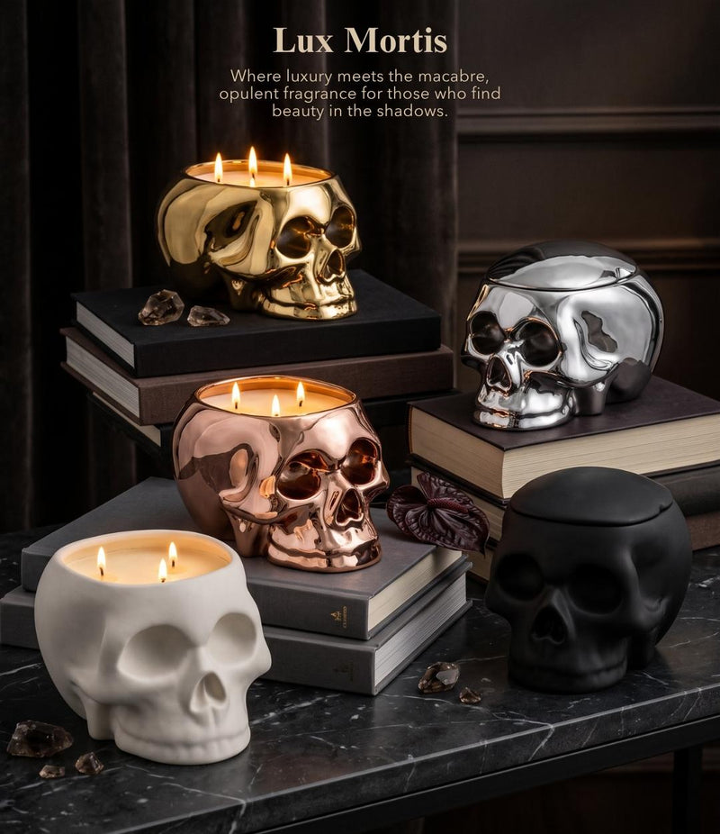 Four skull-shaped candle holders in white, black, rose gold, and gold finishes, styled on stacked books with lit candles against a dark background. Text at the top reads 'Lux Mortis'.