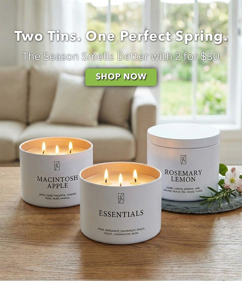 Three candles on a table with promotional text for 'Essentials' candles. Shop 2 for $30 tins.
