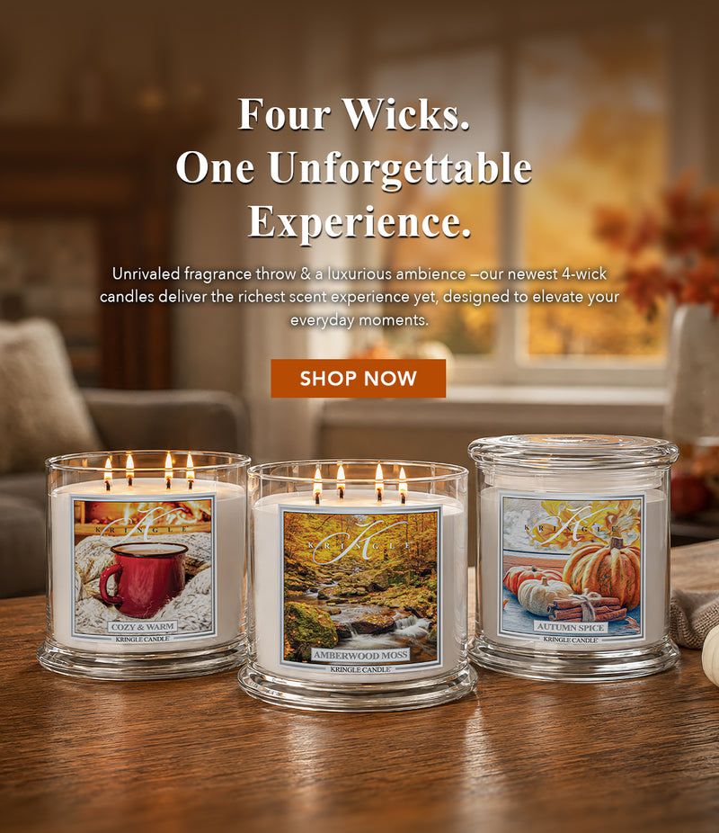 Three lit 4-wick candles in clear glass jars are displayed on a wooden table in a cozy living room setting. The candles feature different autumn-themed scents with illustrated labels: a red mug, a stream, and pumpkins.