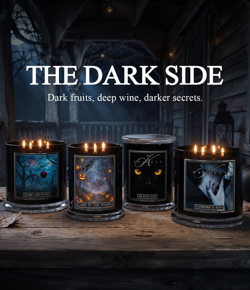 Four lit candles in black glass jars with gothic-themed labels are arranged on a rustic wooden table. Above them, large white text reads 'THE DARK SIDE' with the subtitle 'Dark fruits, deep wine, darker secrets.