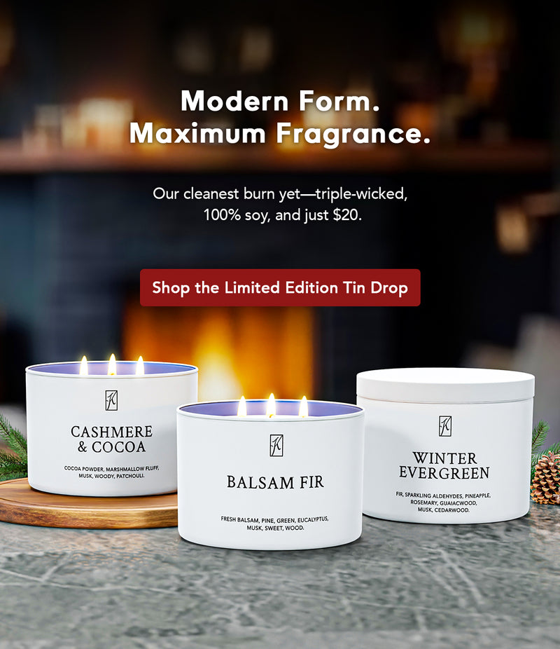 Three candles with labels 'Cashmere & Cocoa', 'Balsam Fir', and 'Winter Evergreen' on a table with a fireplace in the background.