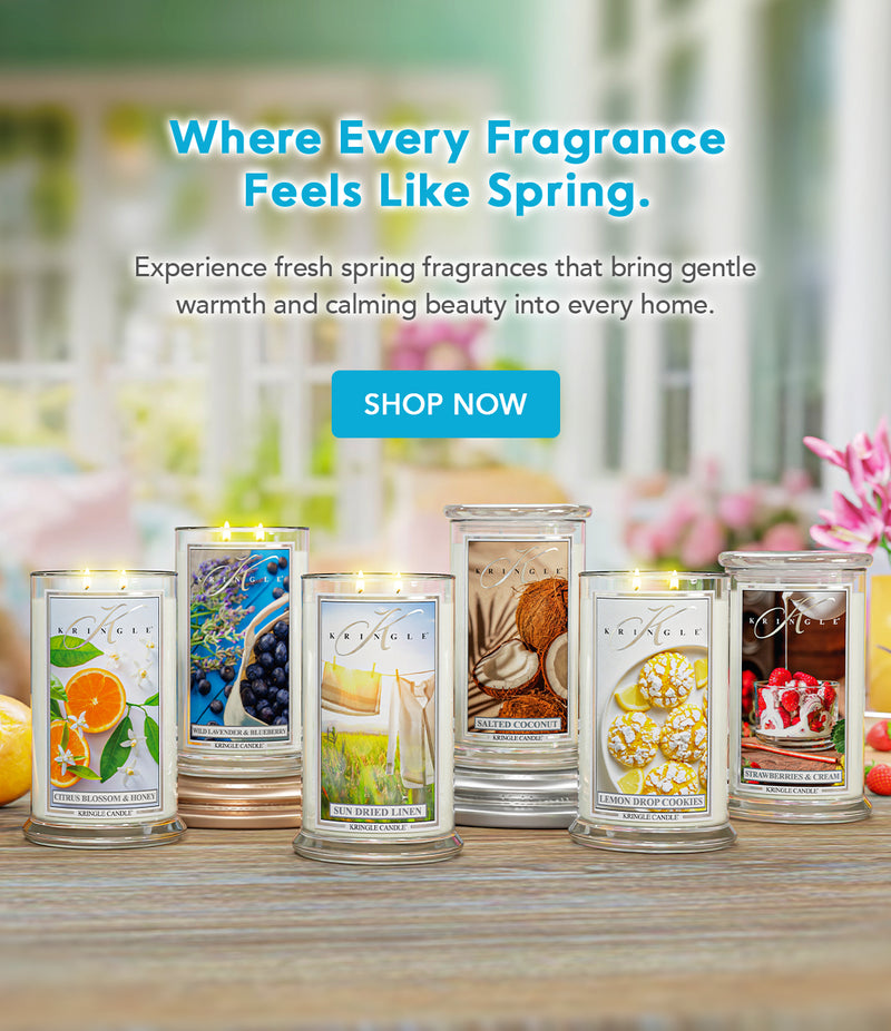 Assorted candles with spring-themed labels on a wooden surface, with a blurred outdoor background.