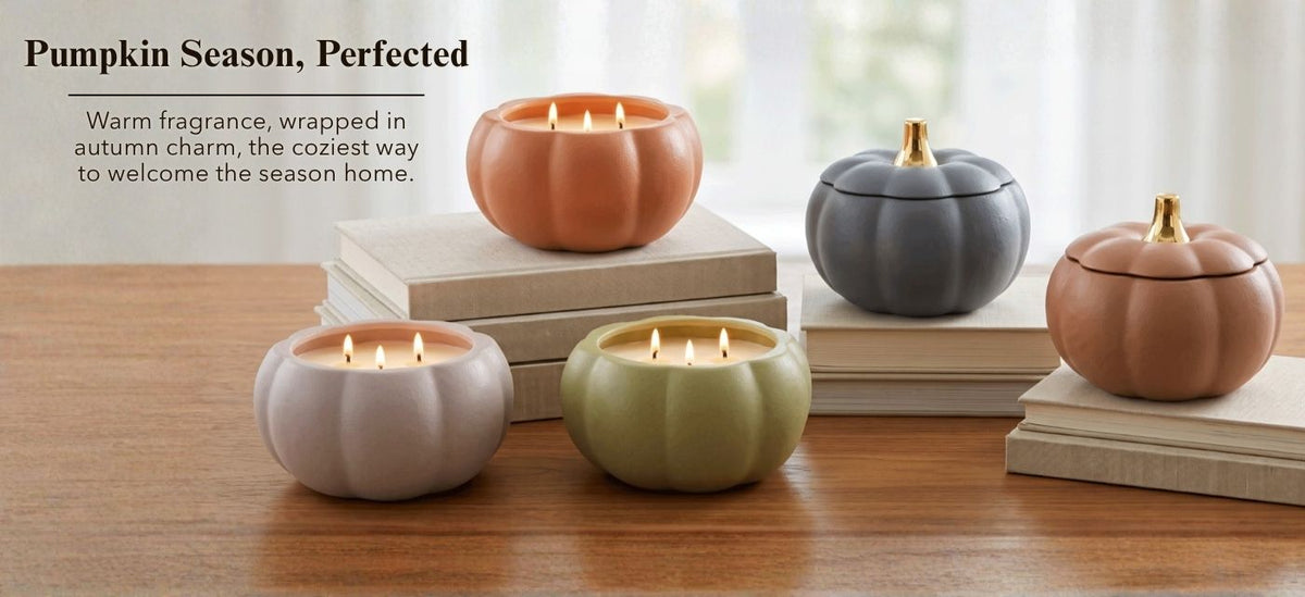 Four pumpkin-shaped candle holders in peach, gray, sage green, and blush pink, arranged on stacked books on a wooden table with a softly lit window in the background. Text on the left reads, 'Pumpkin Season, Perfected.