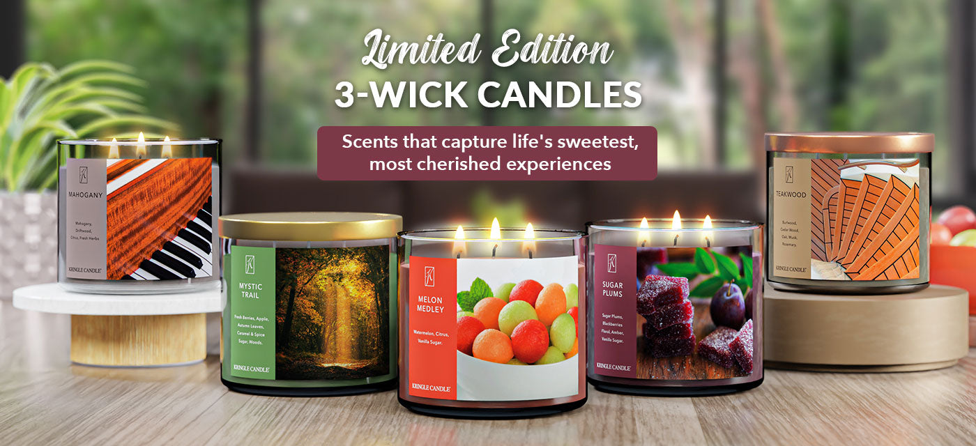 Three-wick candles with colorful labels on a wooden surface, with a blurred natural background.