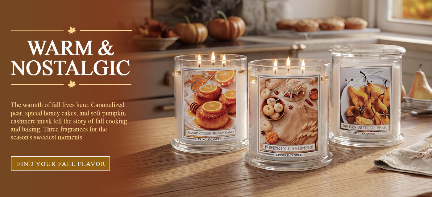 Kringle Candle fall banner featuring three 3-wick candles — Orange Ginger Honey Cakes, Pumpkin Cashmere, and Brown Butter Pear — on a wooden kitchen counter with pumpkins and muffins, with text 'Warm & Nostalgic' and a 'Find Your Fall Flavor' button.