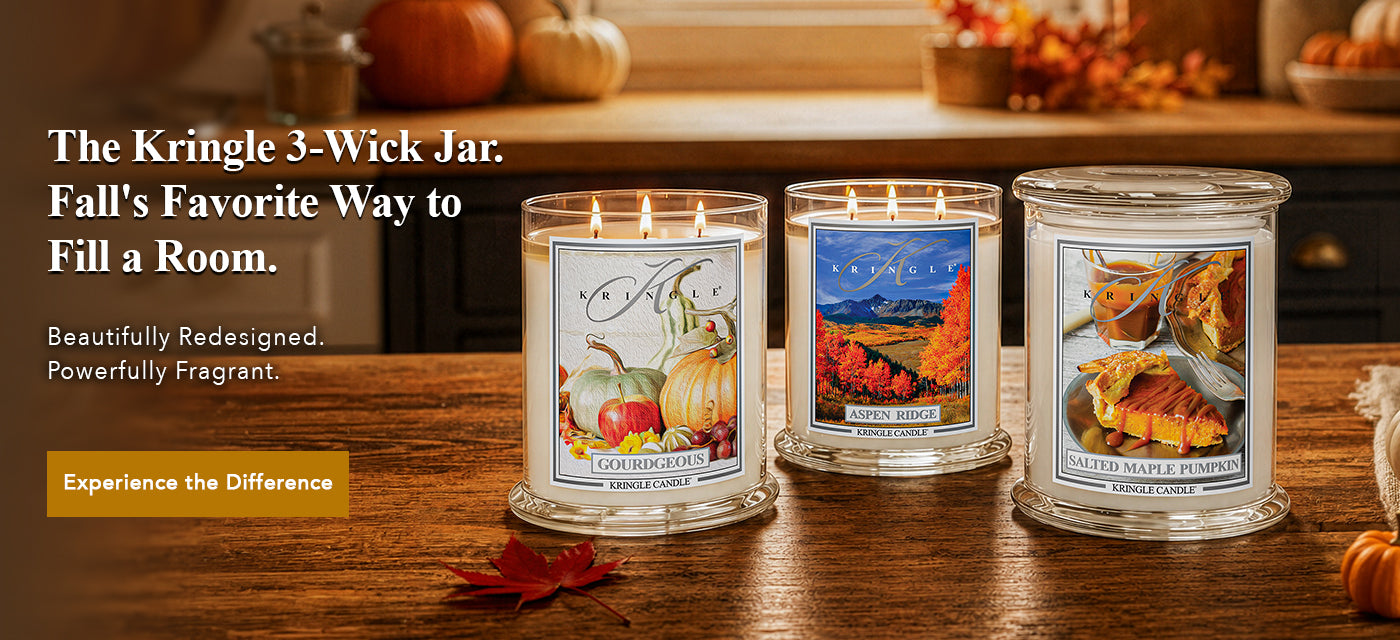 Three lit Kringle 3-wick candles in clear glass jars with autumn-themed labels, displayed on a wooden table with fall decor in the background. Text on the left reads, 'The Kringle 3-Wick Jar.