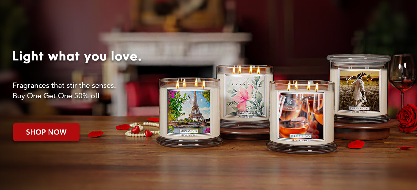 Kringle Candle jars displayed on a wooden table in a warm, romantic setting with glowing flames, featuring the message “Light what you love” and a Buy One Get One 50% off promotion.