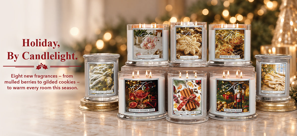 A group of lit glass jar candles with holiday-themed labels arranged on a tabletop, with a blurred Christmas tree and warm bokeh lights in the background. Text on the left reads, 'Holiday, By Candlelight' and describes new fragrances.