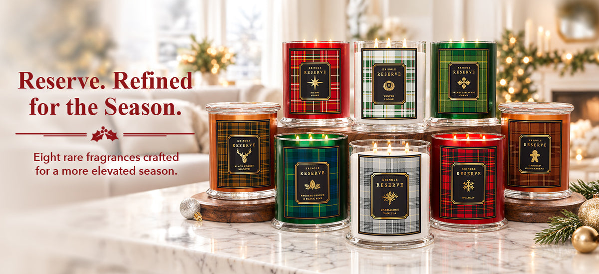 A group of eight scented candles in glass jars with holiday-themed labels and plaid packaging, arranged on a marble surface in a softly lit holiday interior. Text on the left reads, 'Reserve.