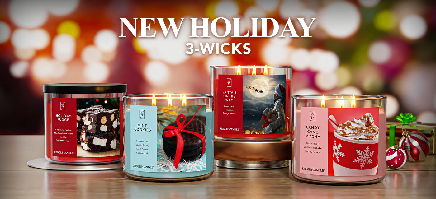 Four '3-Wicks' candles with holiday-themed packaging on a wooden surface, blurred lights in the background.