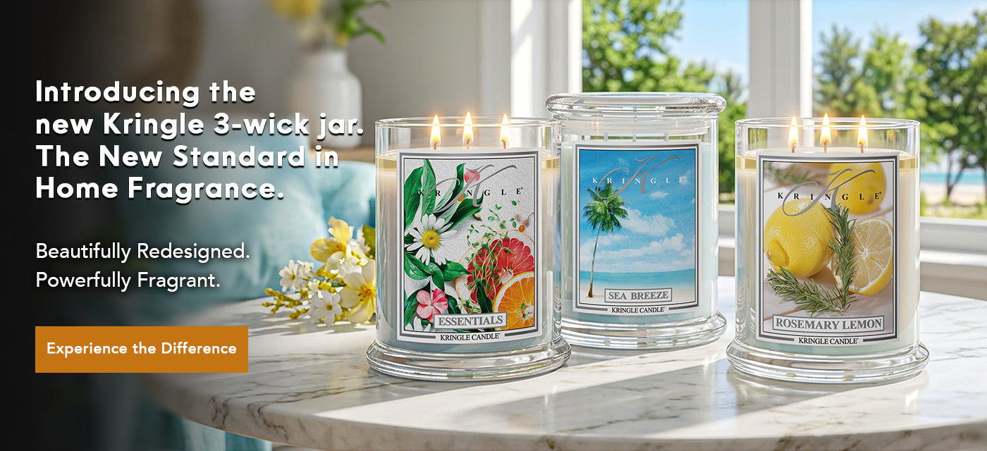 Three Kringle Candle jars on a table with scenic labels, surrounded by flowers and a blurred outdoor view.