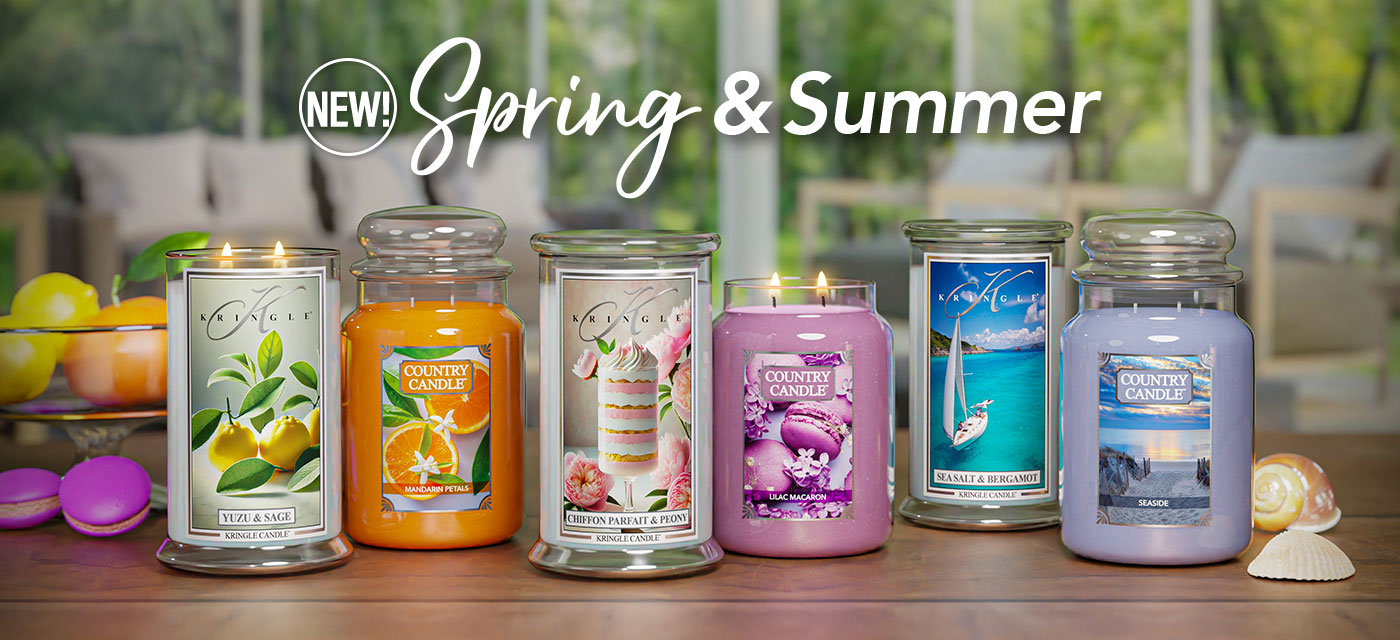 Kringle Candle and Country Candle’s new Spring & Summer collection display. A variety of scented candles in glass jars are showcased on a table with a blurred outdoor background. The candles include scents like Yuzu & Sage, Mandarin Petals, Chiffon Parfait & Peony, Lilac Macaron, Sea Salt & Bergamot, and Seaside. Bright, summery colors and decorative elements such as macarons, citrus fruits, and seashells complement the scene.