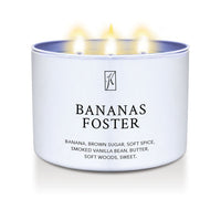 Candle in a container labeled 'Bananas Foster' with a logo on a white background