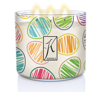 A lit Kringle Candle in a wide, clear jar decorated with colorful Easter egg illustrations. The eggs feature vibrant, hand-drawn-style stripes in colors like teal, orange, pink, purple, yellow, and green. The center of the jar displays the classic Kringle “K” logo. The background is white, emphasizing the cheerful, playful holiday design.