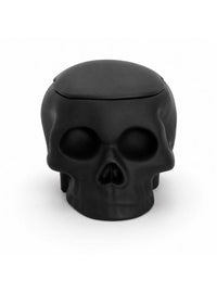A matte black skull-shaped container with a fitted lid, photographed against a seamless white background.