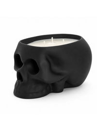 A black skull-shaped candle holder filled with white wax and three wicks, photographed on a clean white background.