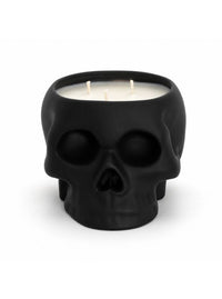 A black skull-shaped candle with three white wicks, set against a plain white background.