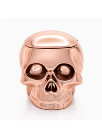 A metallic rose gold skull-shaped container with a hinged lid, shown on a clean white background.