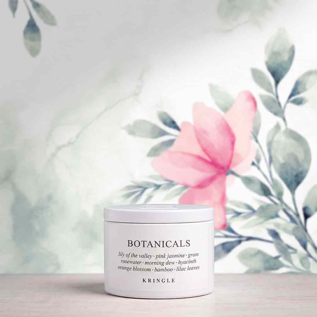 A white jar of KRINGLE Botanicals body wash with a white lid, set on a light wooden surface against a watercolor background of green leaves and a pink flower.