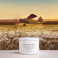 A white jar of KRINGLE 'Far, Far, Away' body butter sits on a light surface in the foreground, with a blurred background of a vintage airplane landing in a grassy field at sunset.