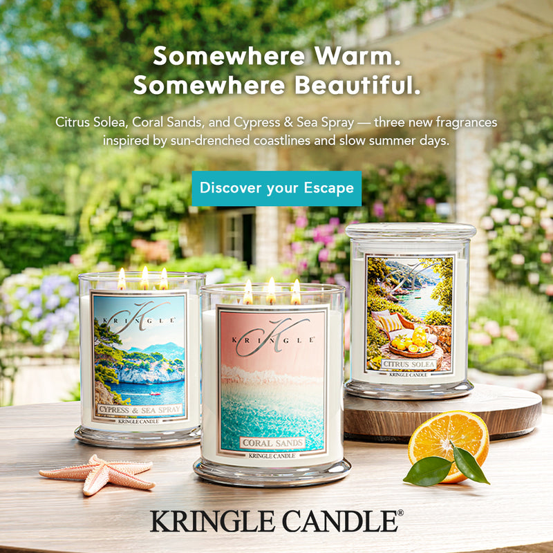 Kringle Candle candles with scenic labels on a table outdoors, featuring citrus and coastal scents.