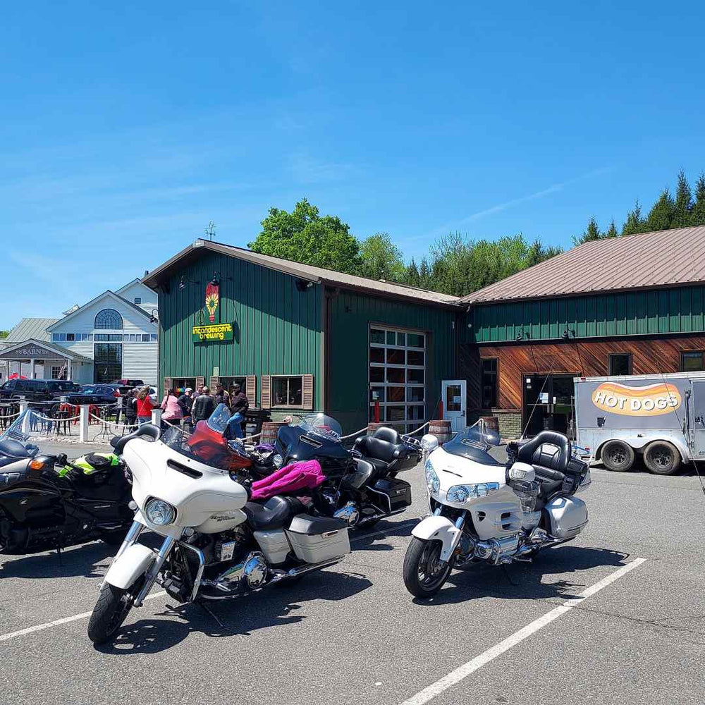 Exterior view of Incandescent Brewing, a green industrial-style building with a roll-up garage door, outdoor seating.