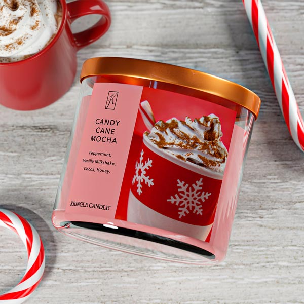 Kringle Candle Candy Cane Mocha candle with a red mug of hot chocolate and candy canes on a wooden surface.